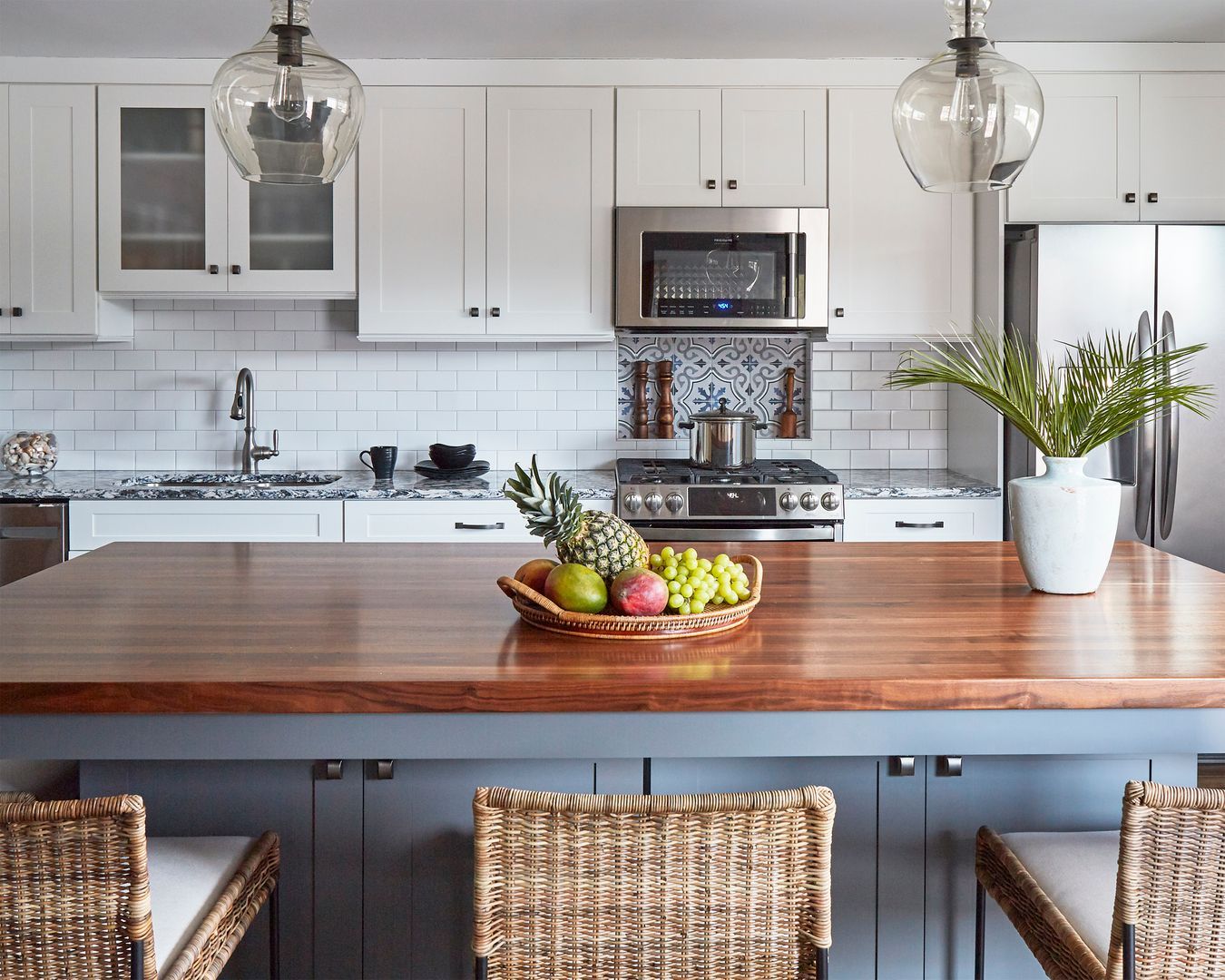 Modern kitchen with white cabinets, subway tile, wooden island, wicker stools, and a fruit bowl centerpiece