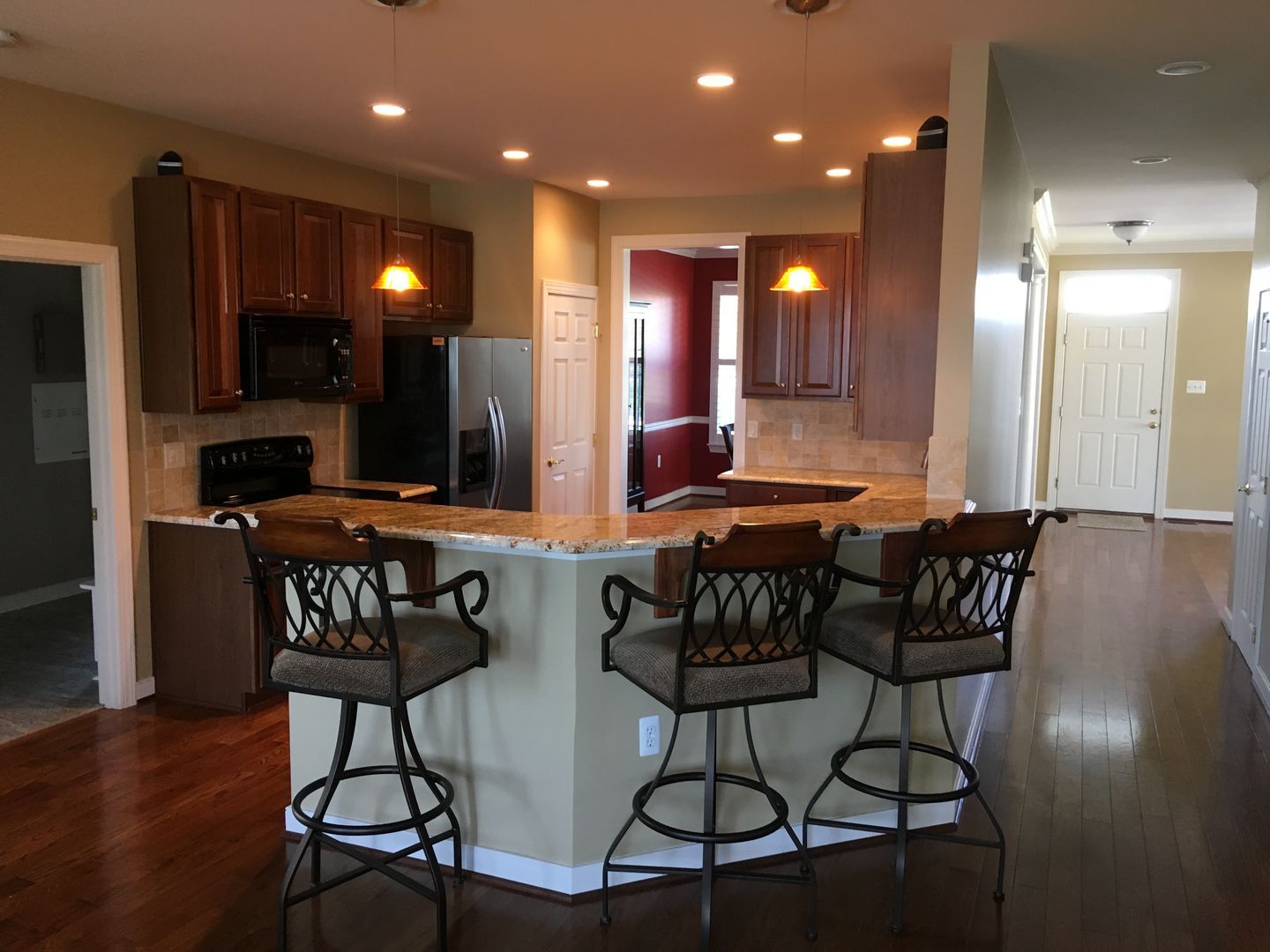 Bright kitchen with wood floors, granite island, bar stools, and warm recessed lighting.