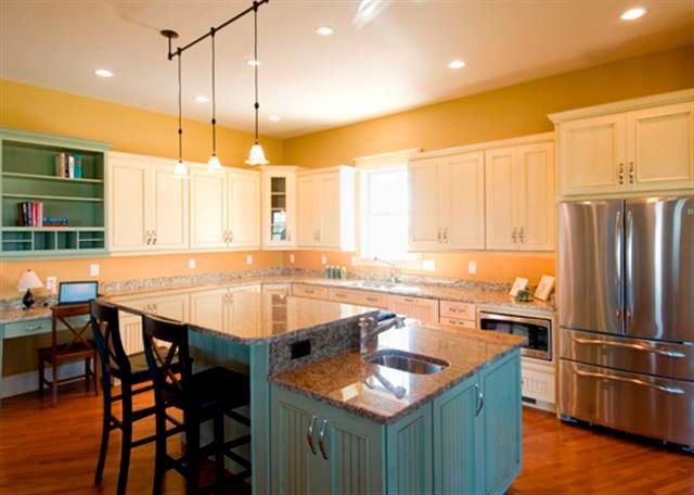 Spacious modern kitchen with white cabinets, granite island, stainless steel fridge, and warm wood floors