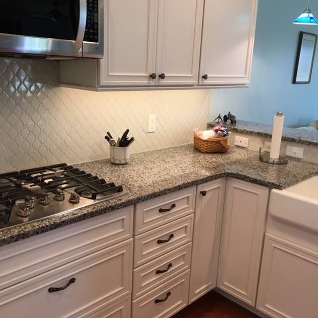 Bright kitchen corner with granite countertop, gas stove, white cabinets, and small decor items