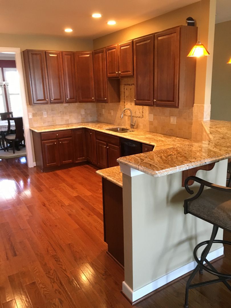 Warm kitchen with dark wood cabinets, granite counters, and polished hardwood floors, plus a breakfast bar.