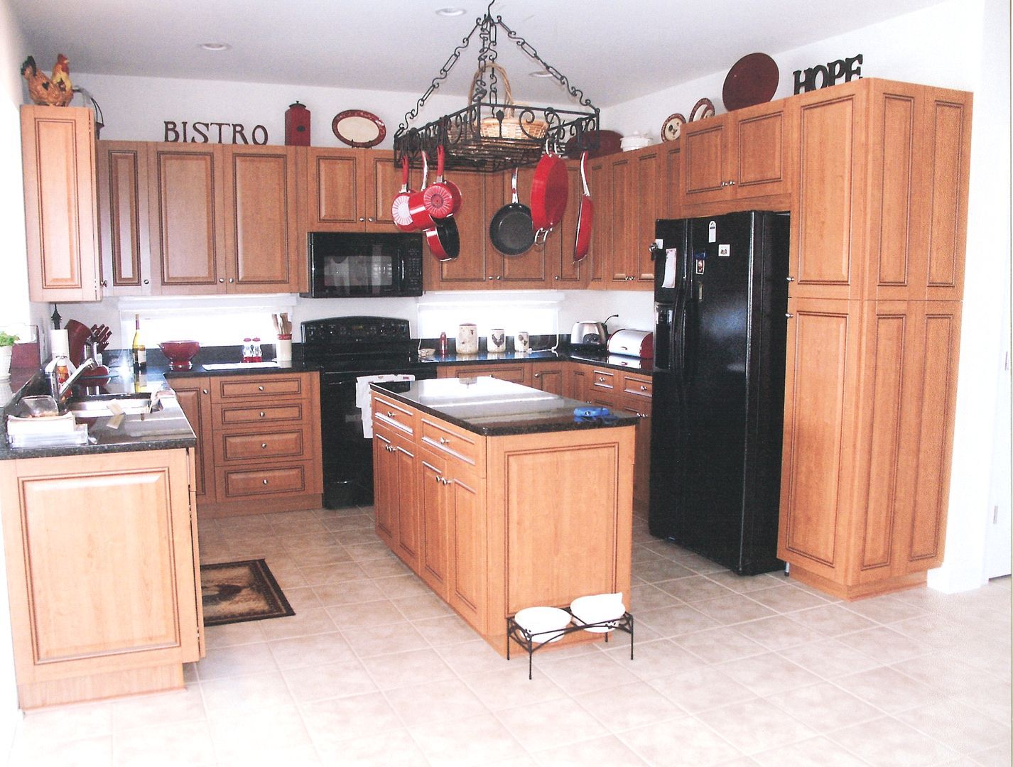 Spacious kitchen with wooden cabinets, black appliances, central island, and decorative wall signs.