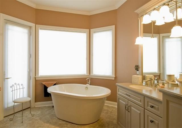 Bright beige bathroom with a freestanding tub, vanity, large windows, and chandelier lighting