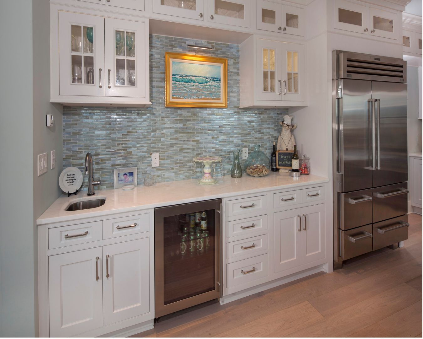 Bright white kitchen with blue mosaic backsplash, stainless refrigerator, and glass-front cabinets