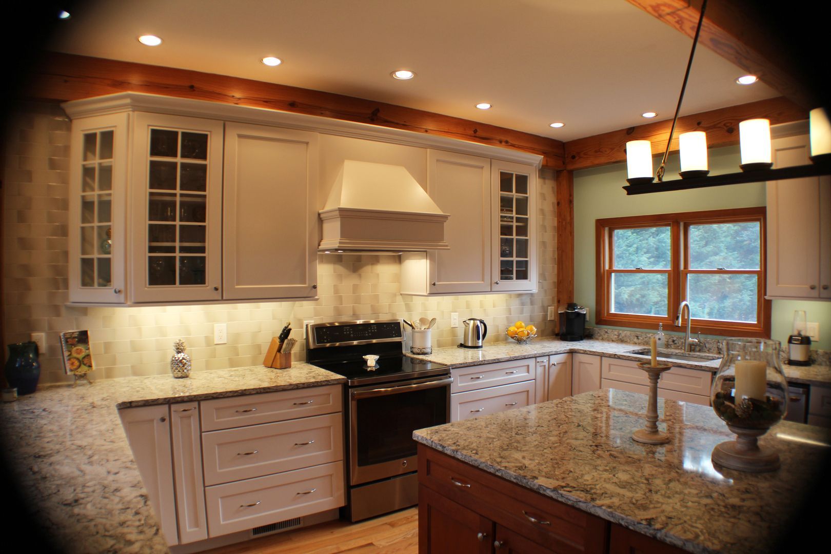 Modern kitchen with cream cabinets, granite island, stainless stove, and large windows.