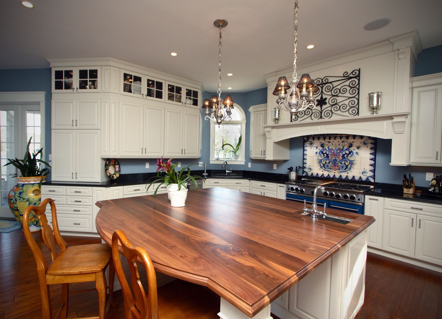 Bright kitchen with large wooden island, white cabinets, black countertops, and chandelier lighting.