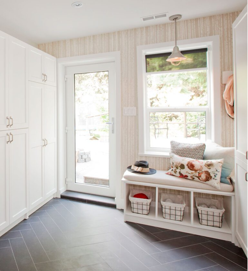 Bright mudroom with white cabinets, bench seating, window, and gray floor in a light wood-paneled entryway