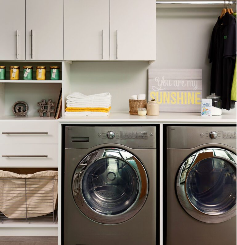 Laundry room with two front-loading washers, white cabinets, folded towels, and decorative shelves