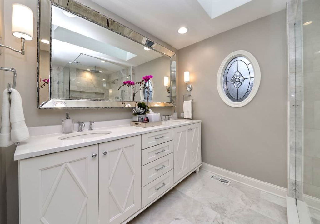 Bright bathroom with double vanity, large mirror, glass shower, and round wall clock on beige wall