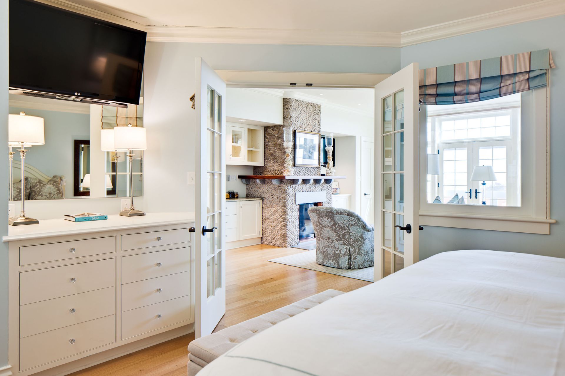 Bright bedroom with white dresser, wall-mounted TV, and view into a kitchen