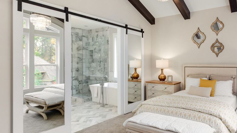Bright bedroom with bed, bedside tables, sliding glass doors, and an en suite bathroom visible through the glass.