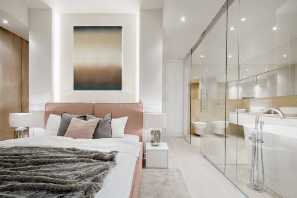 Modern bedroom with a pink bed, gray throw, and glass wall opening to a bright bathroom