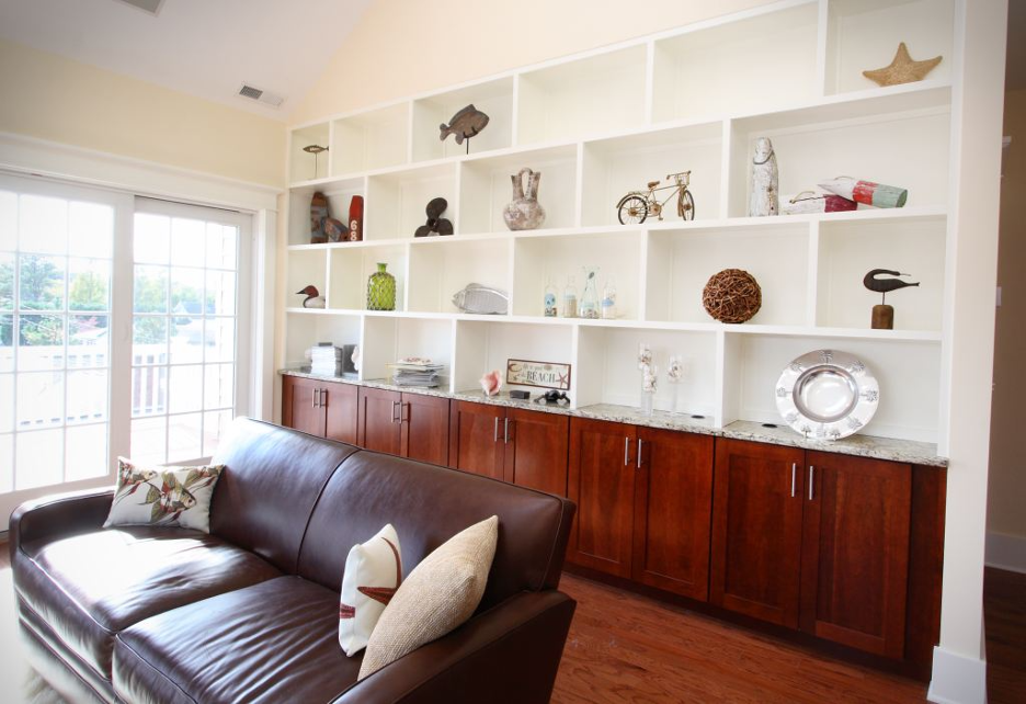 Bright living room with brown leather sofa and white built-in shelves filled with decor above wood cabinets