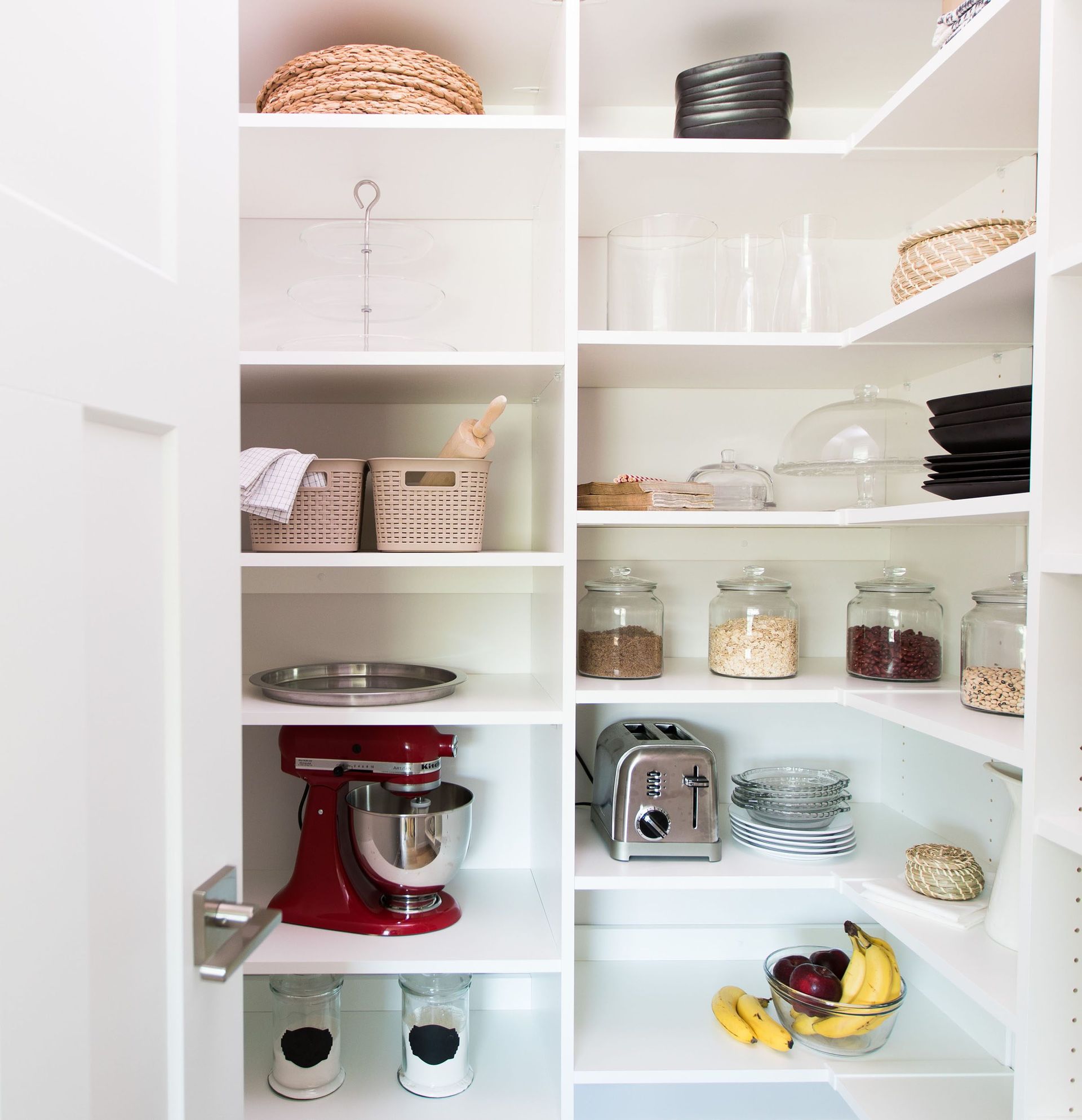 Open pantry with white shelves holding dishes, jars, appliances, and a red stand mixer