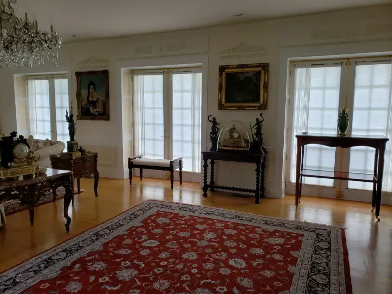 Elegant living room with a red patterned rug, hardwood floors, large windows, dark wood furniture, and framed paintings.