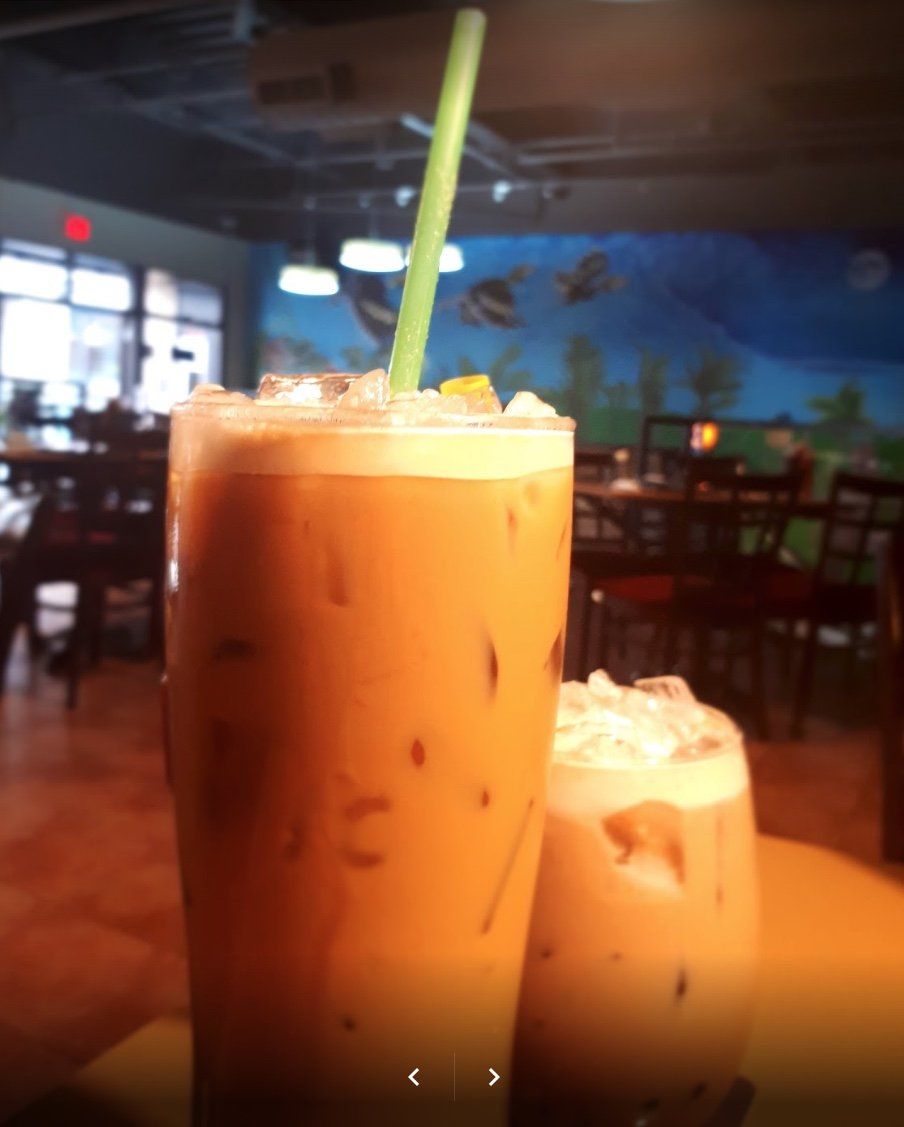 Iced Thai tea in two glasses with a green straw, in a restaurant setting.