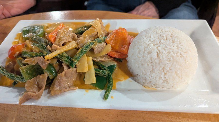 Yellow curry with vegetables and pork, served with a scoop of white rice on a white rectangular plate.