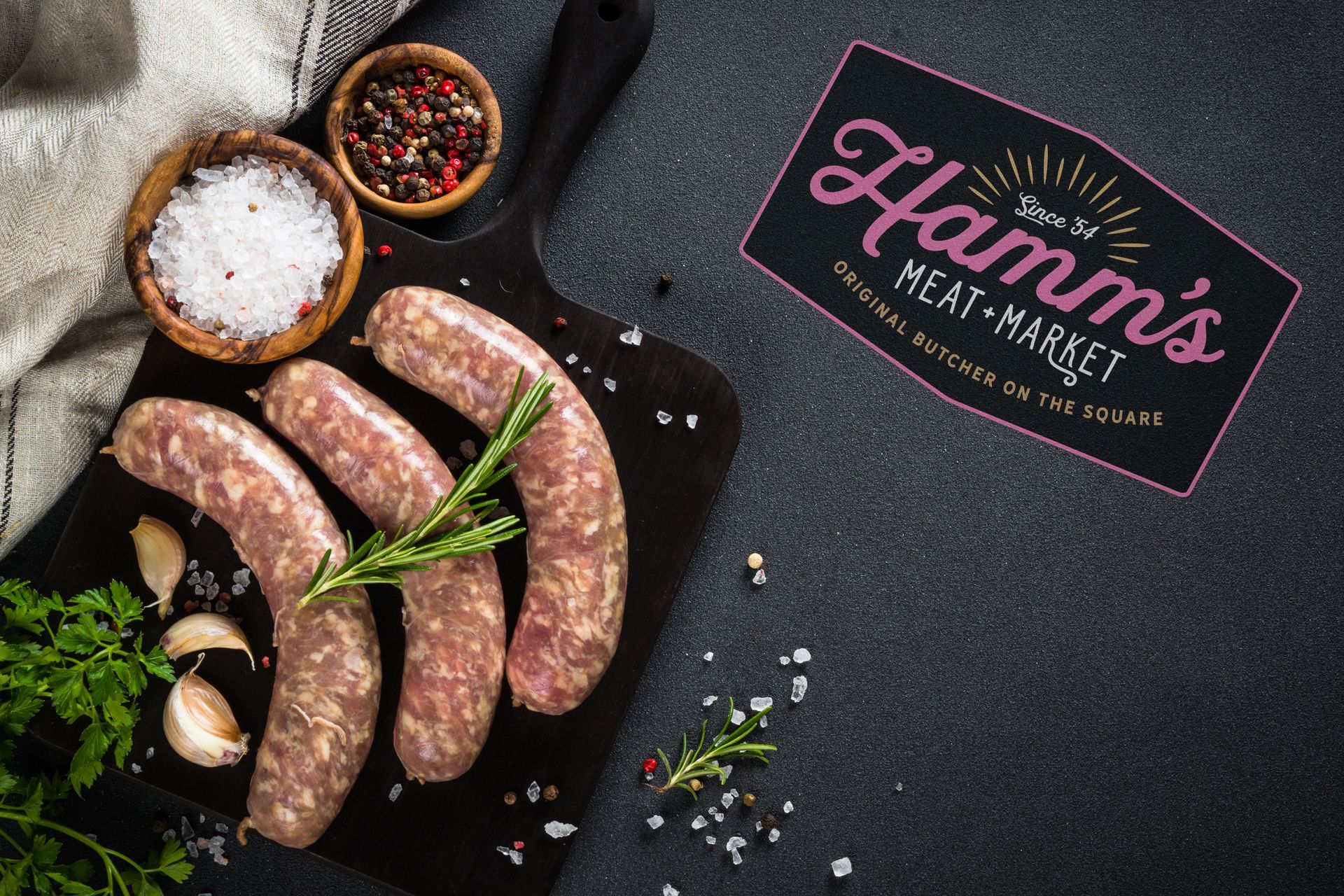Raw sausages on a cutting board with a hamm 's meat market sign in the background.