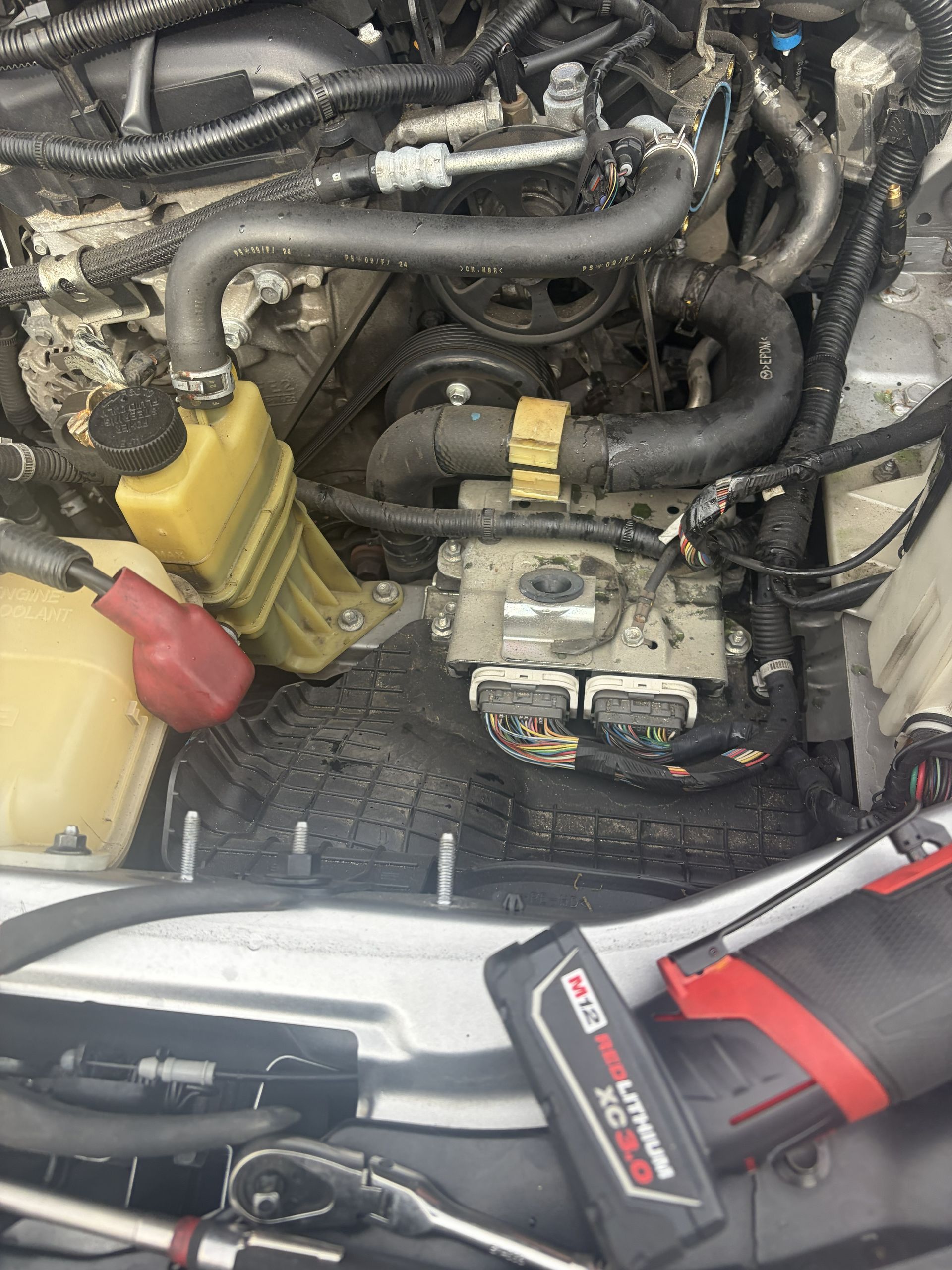 Car engine bay with yellow and red jumper cable clamps connected near the battery.