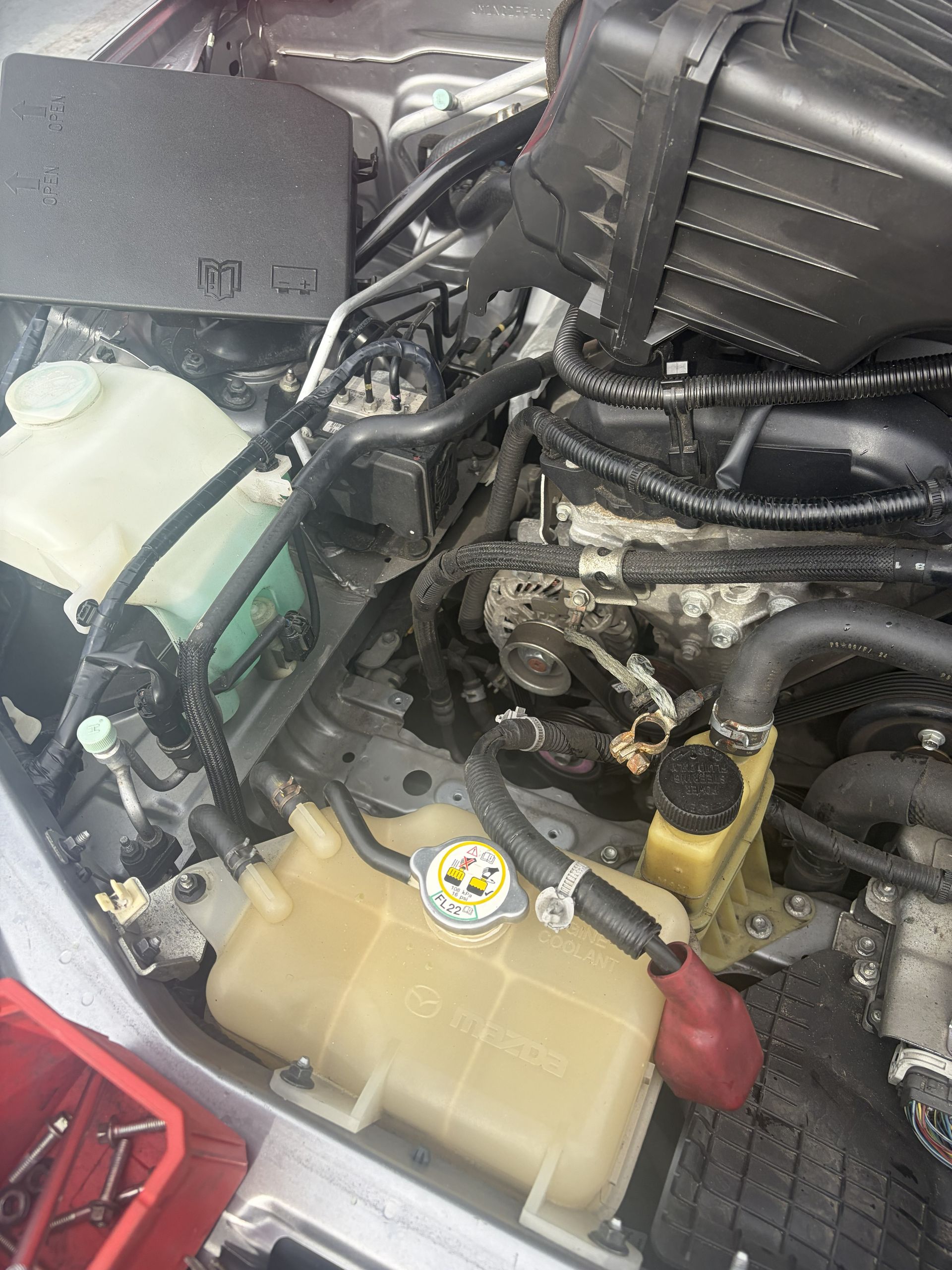Close-up of a car engine bay with coolant reservoir, hoses, and wiring visible