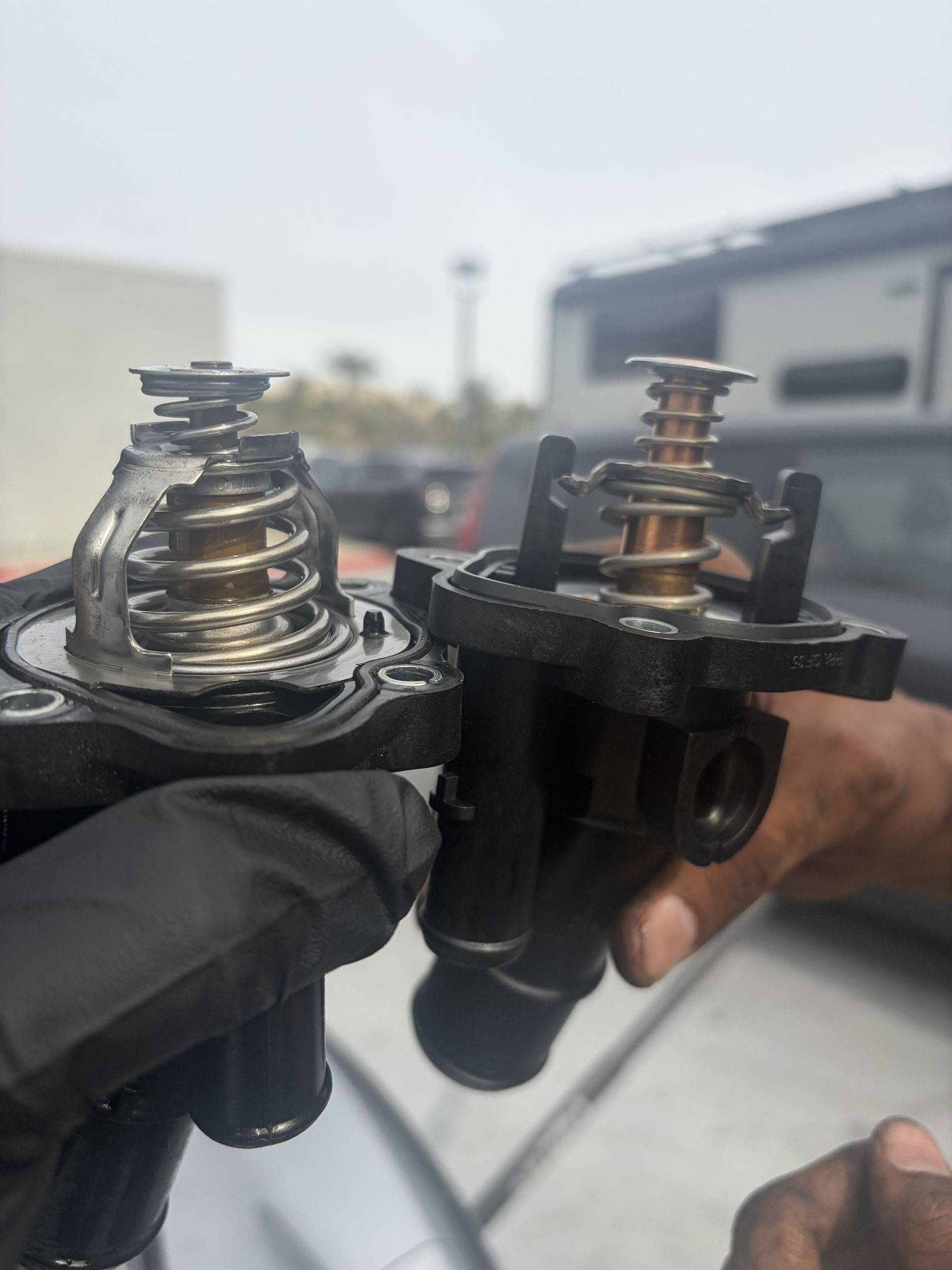 Two damaged black plastic valve assemblies held in gloved hands outdoors, with broken springs exposed