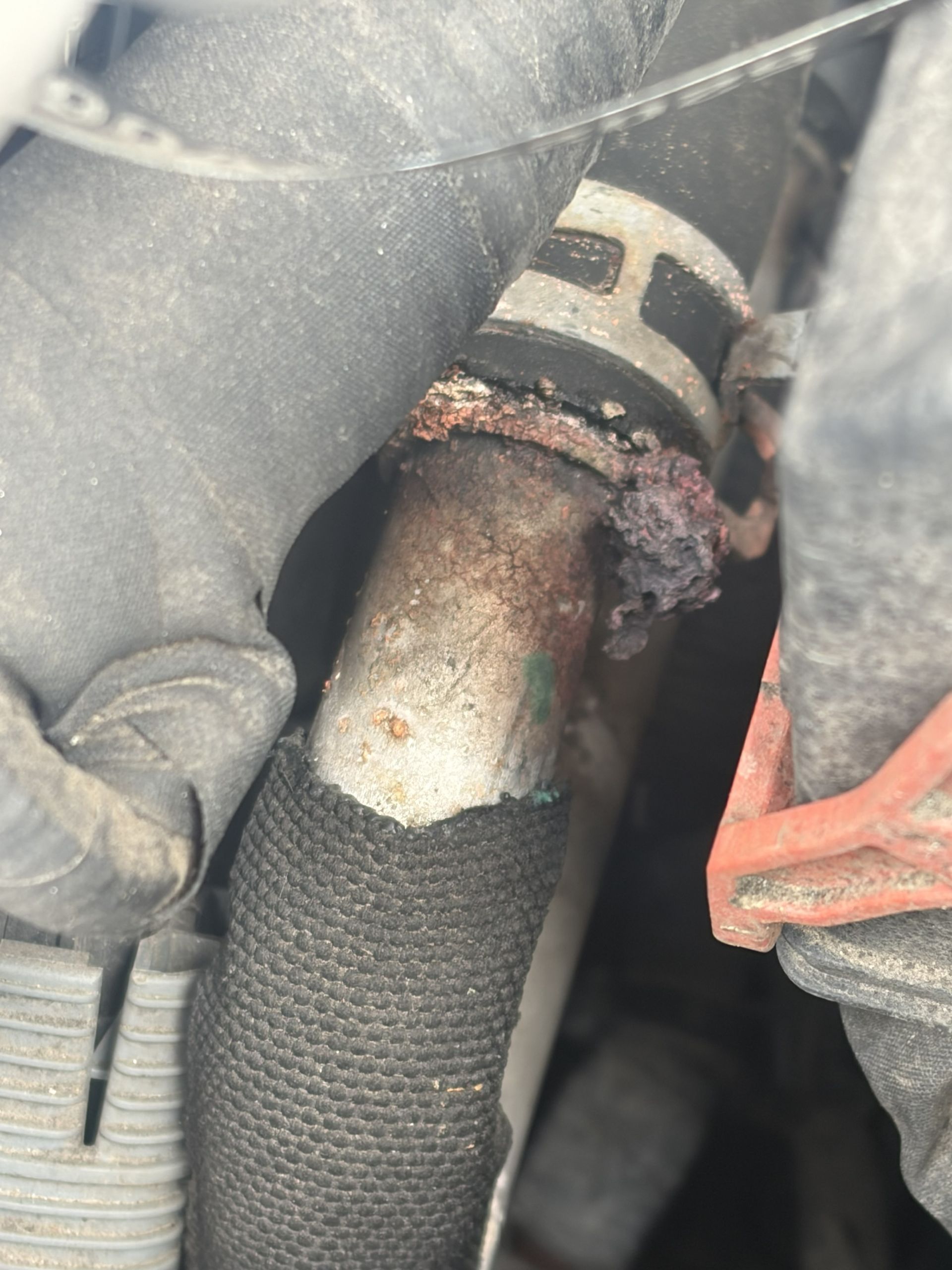 Close-up of a corroded metal hose fitting with a black braided line and rust buildup inside an engine bay
