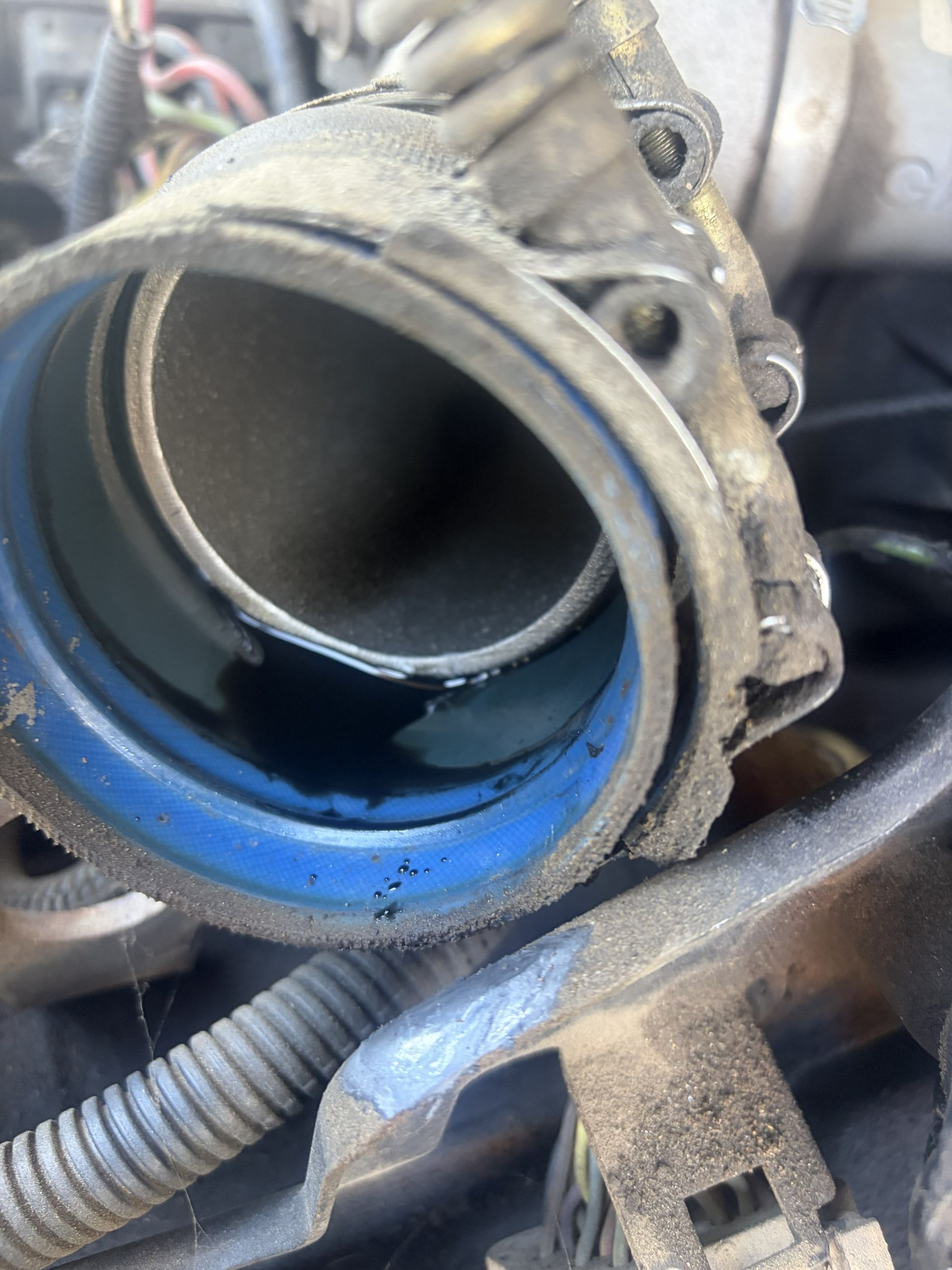 Close-up of a car engine intake hose with blue residue around the opening and clamp hardware nearby