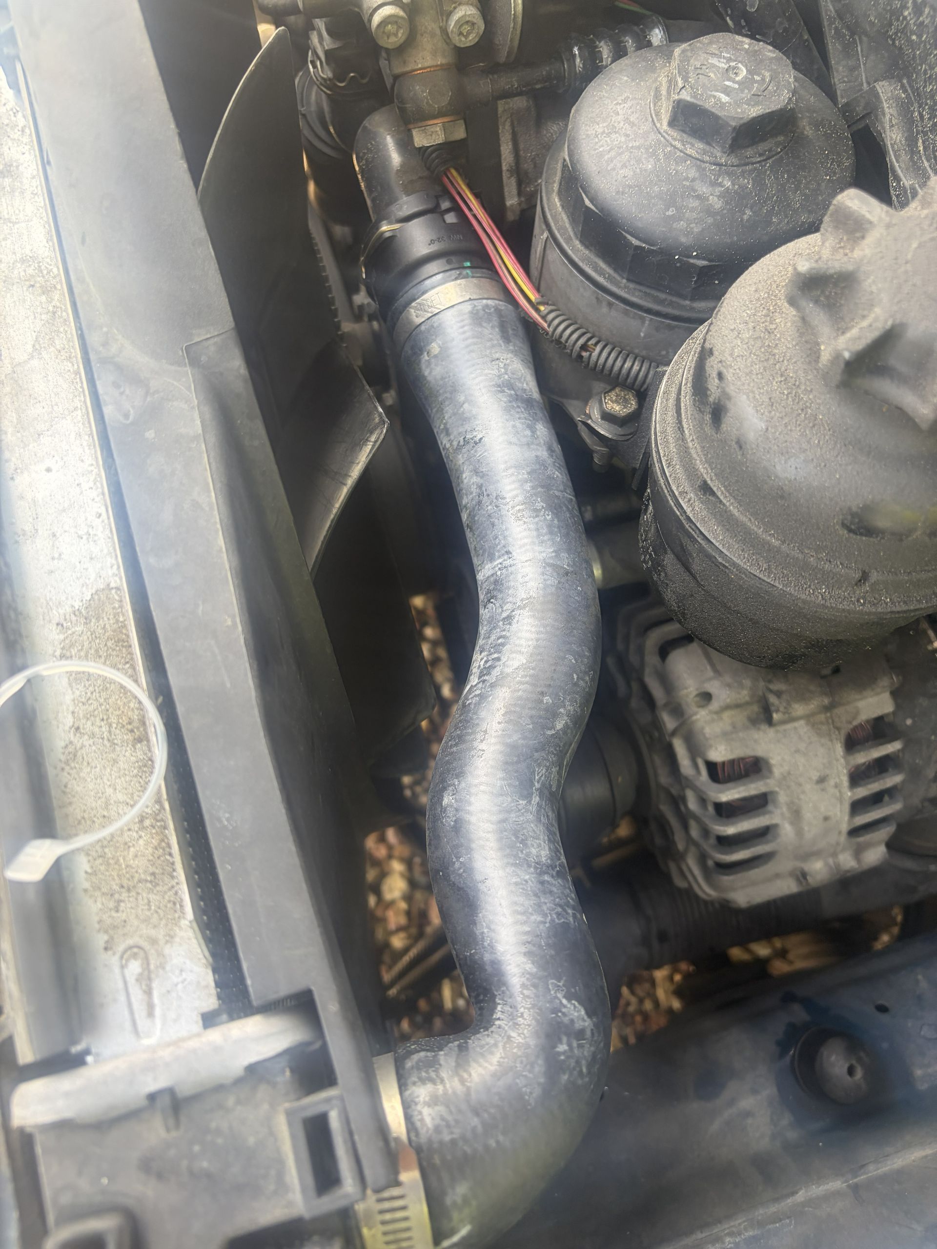 Close-up of a car engine bay with a black hose, wiring, and metal components covered in grime.
