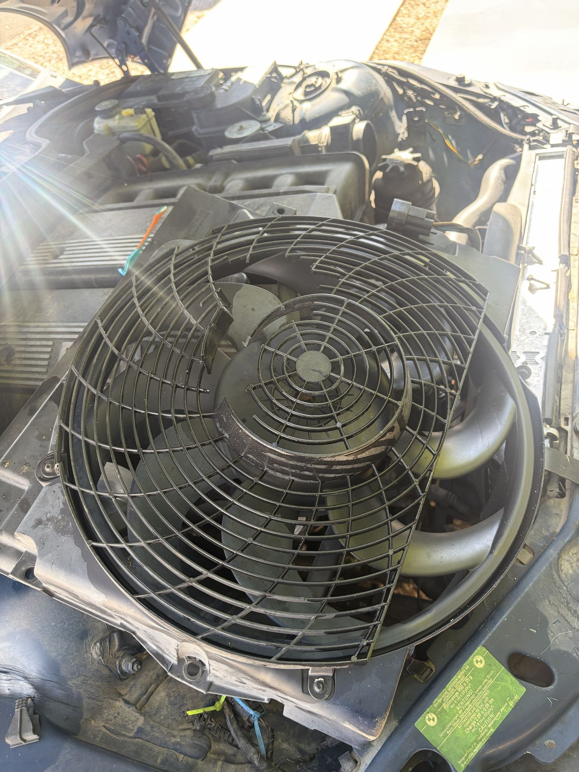 Close-up of an engine bay with a large black cooling fan and hoses under bright sunlight.