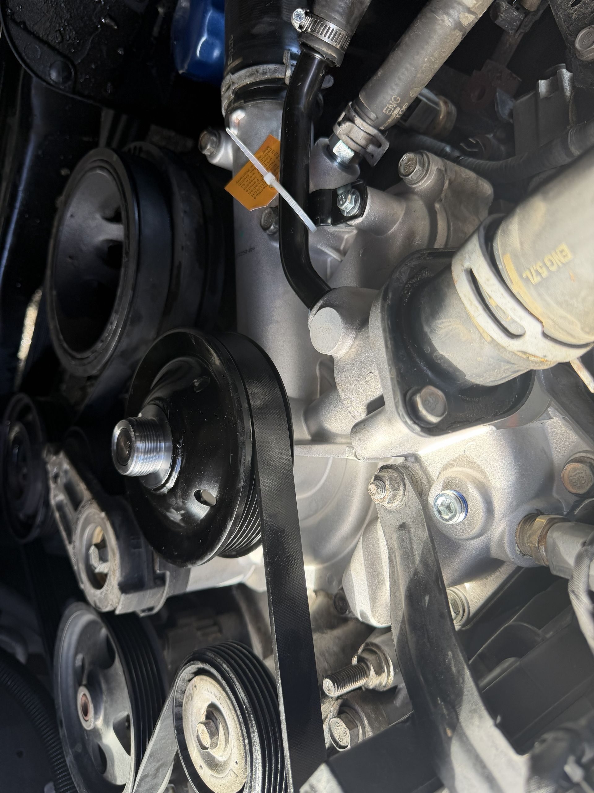 Close-up of a car engine with black pulleys, belts, and hoses under the hood