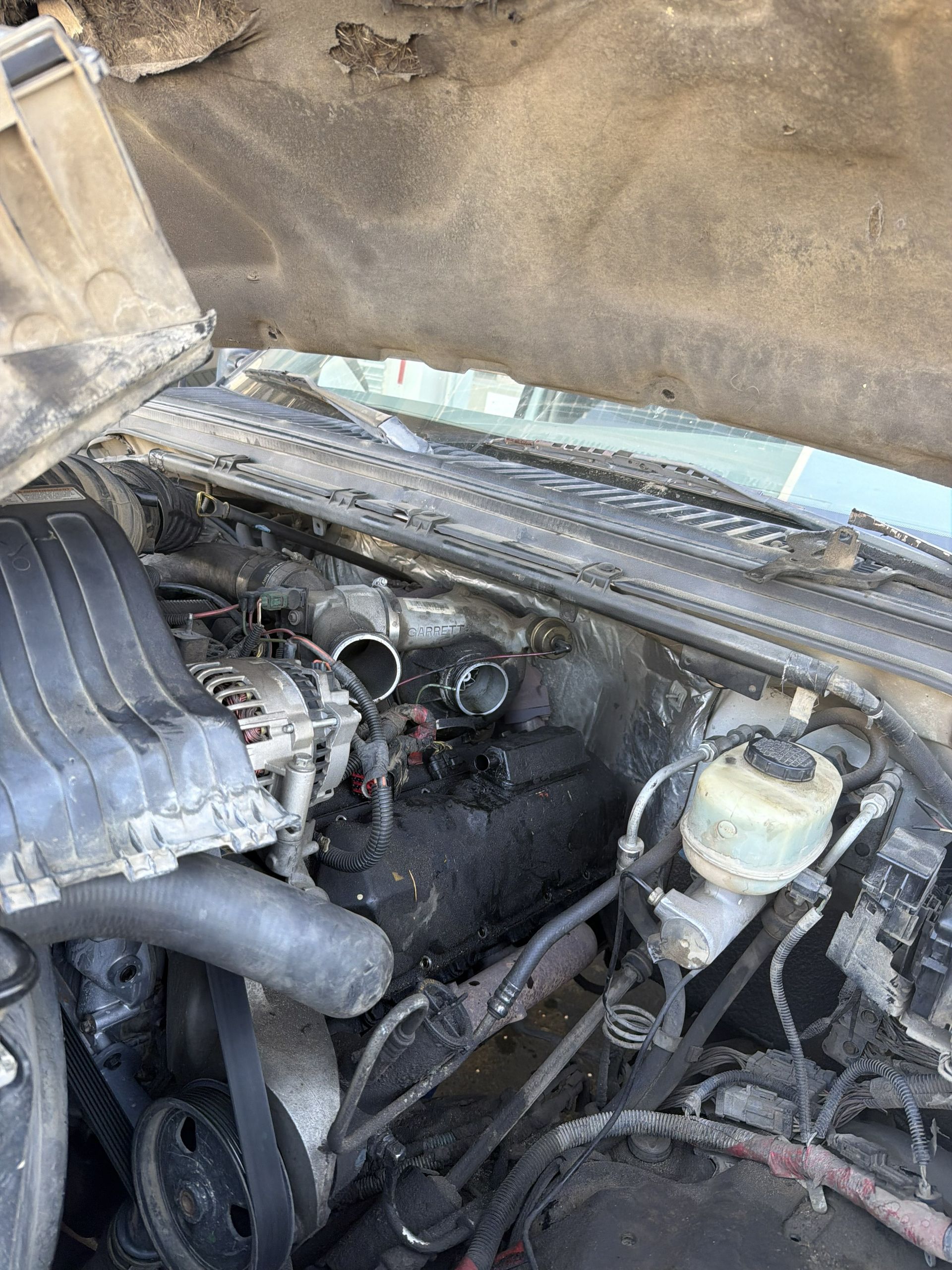 Open car engine bay with hoses, belts, and dusty components under the hood.
