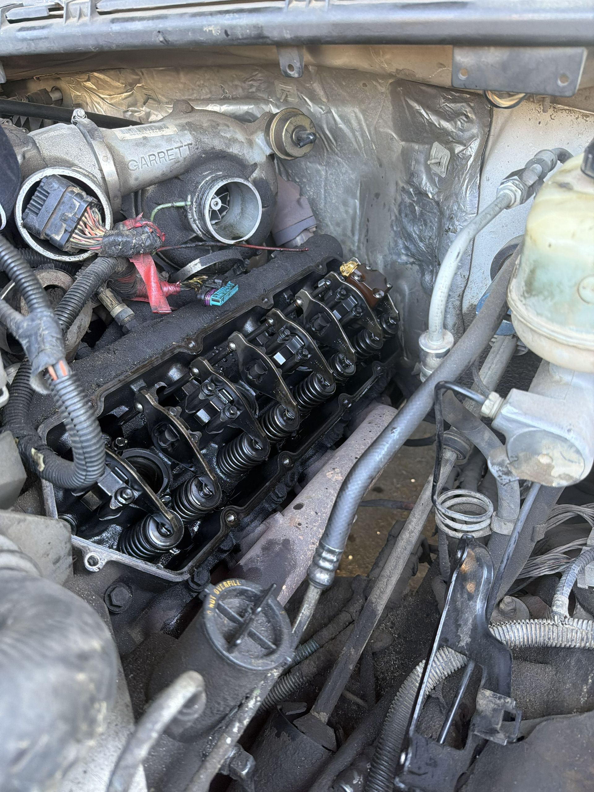 Car engine bay with exposed black valve cover and hoses during repair
