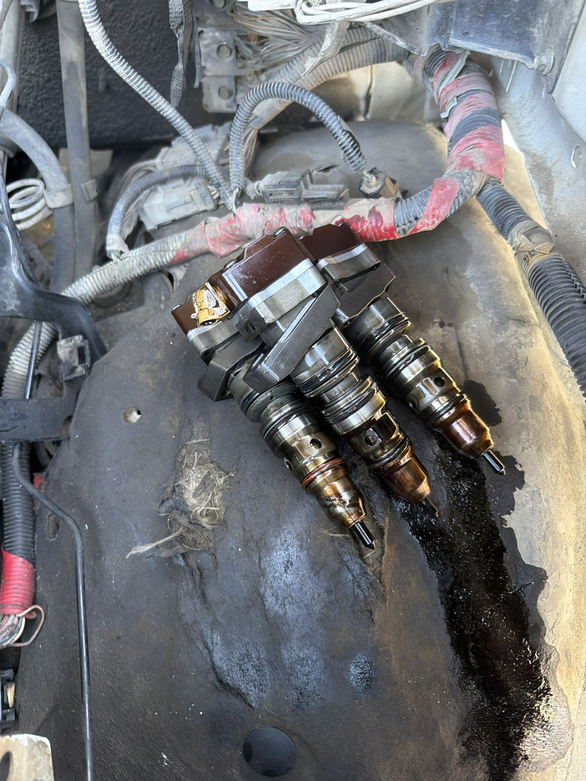 Fuel injector assembly covered in black sludge and residue inside an engine compartment