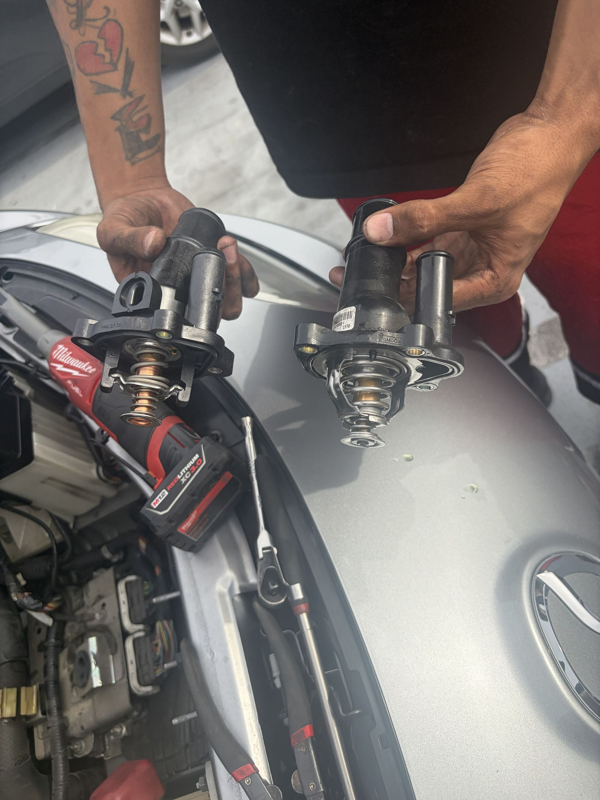 Hands holding two motorcycle parts above a silver bike tank and red-and-black motorcycle seat