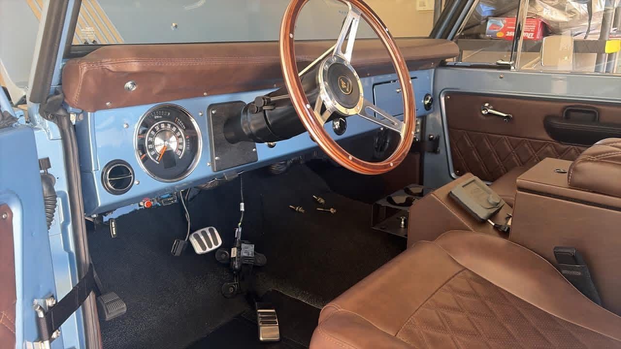 Interior of a vintage blue car with brown leather seats, wooden steering wheel, and dashboard controls