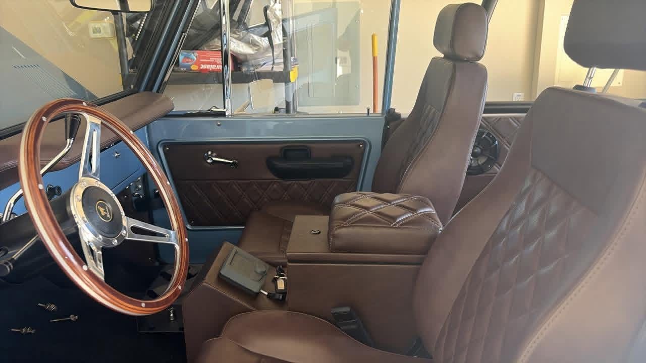 Vintage car interior with tan seats, wood steering wheel, and a center console