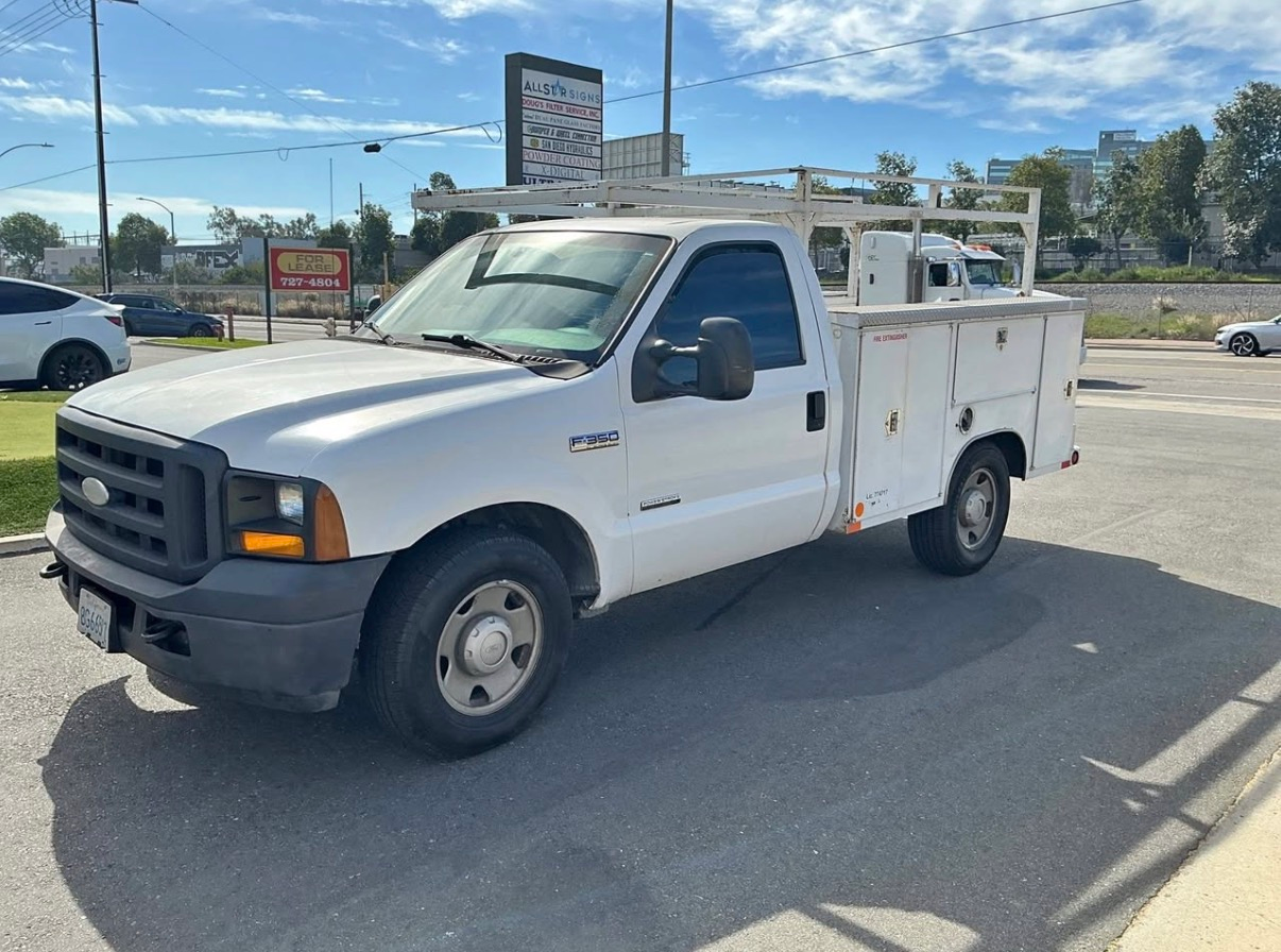 White utility truck parked in a lot on a sunny day, with a blue sky and road signs in the background