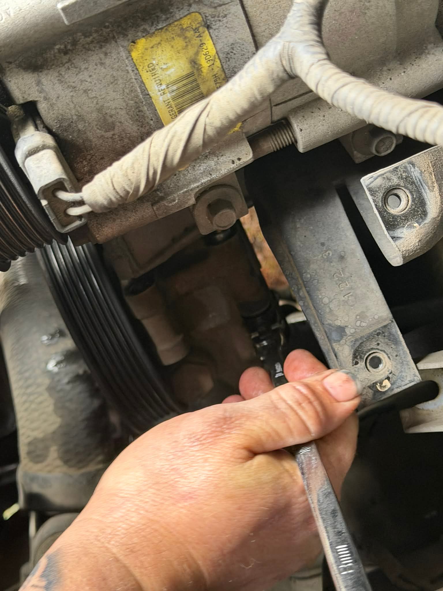 Hand using a wrench to loosen a bolt on a car engine bracket near a serpentine belt