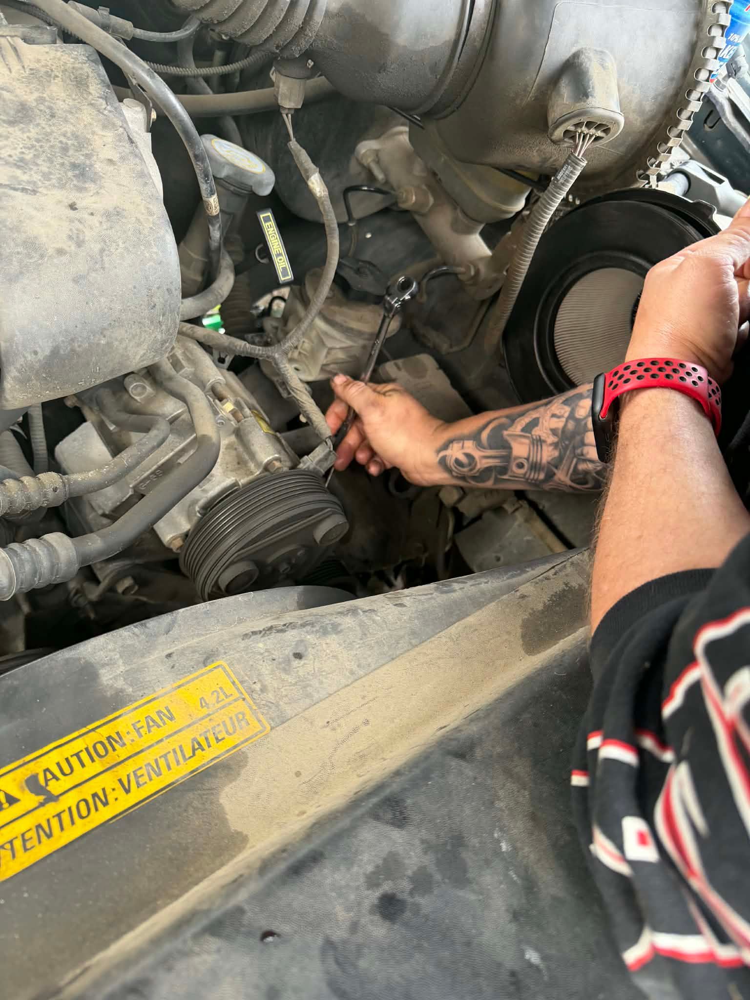 Person reaching into an engine bay to adjust a component, with tattooed arm visible.