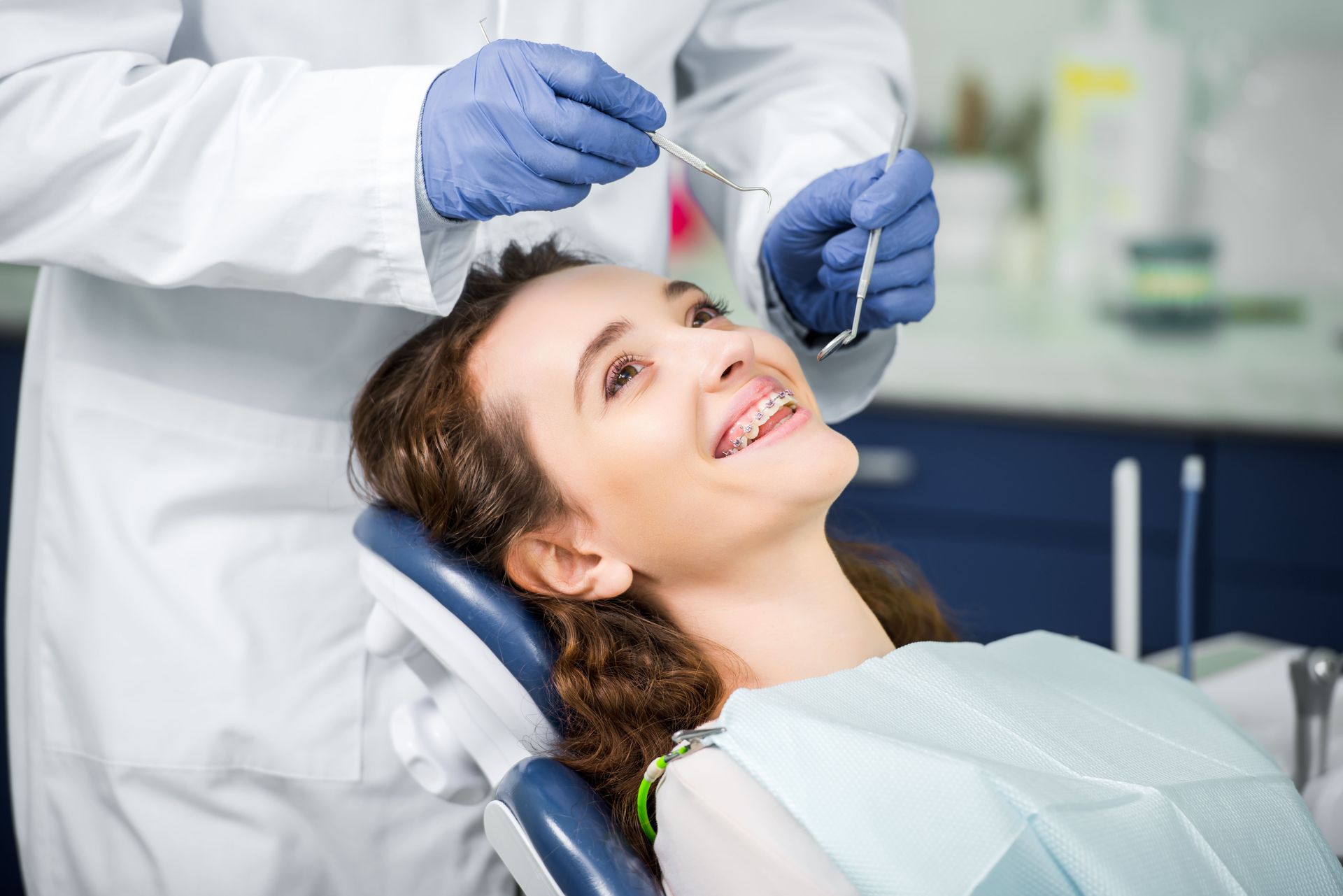 Uma mulher em uma cadeira odontológica sorri enquanto um dentista examina seus dentes.