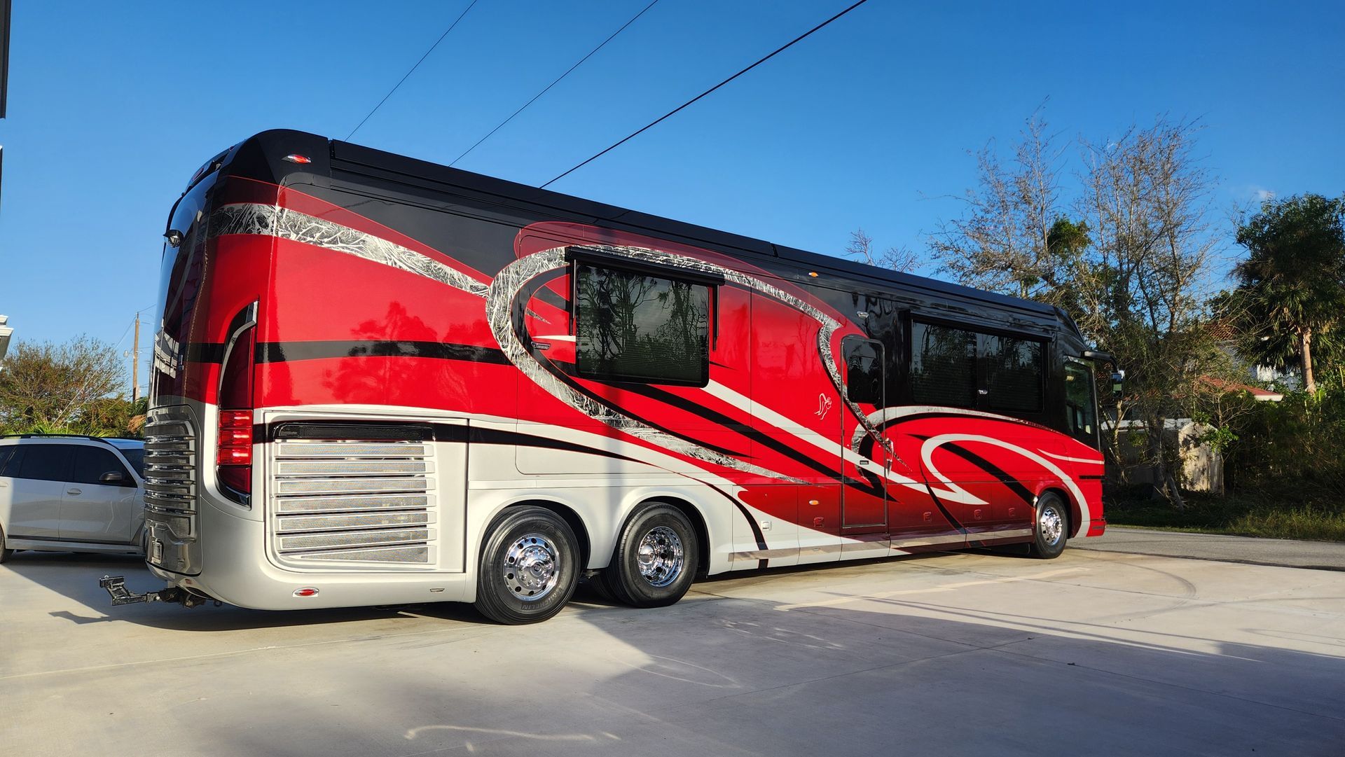 Red and silver luxury RV with stylized graphics parked outdoors on a sunny day.