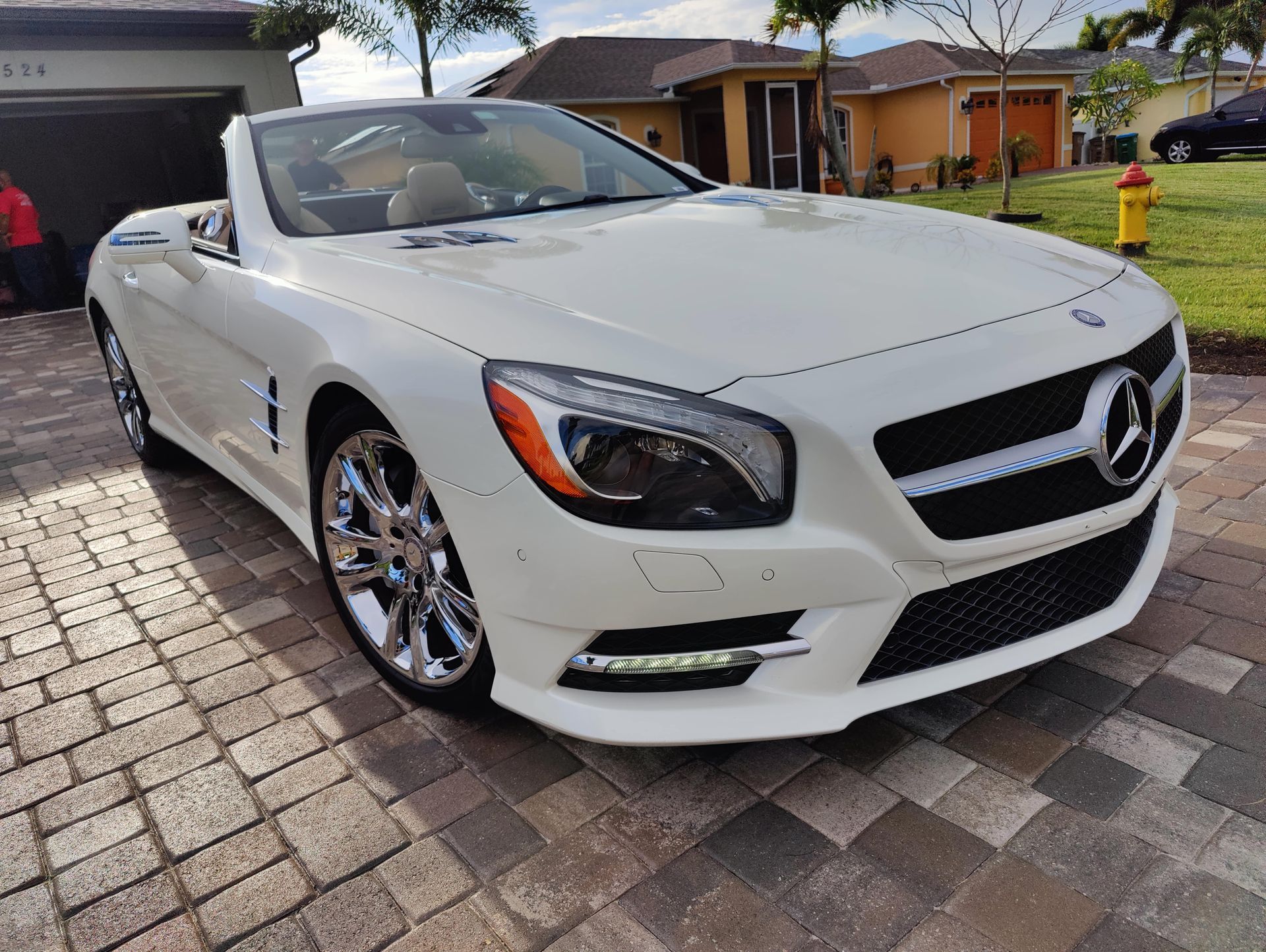 White Mercedes convertible parked on a brick driveway, sunny day.