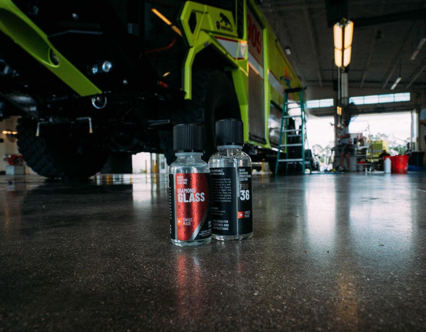 Two bottles of car detailing products on a concrete floor in a garage with a yellow fire truck.