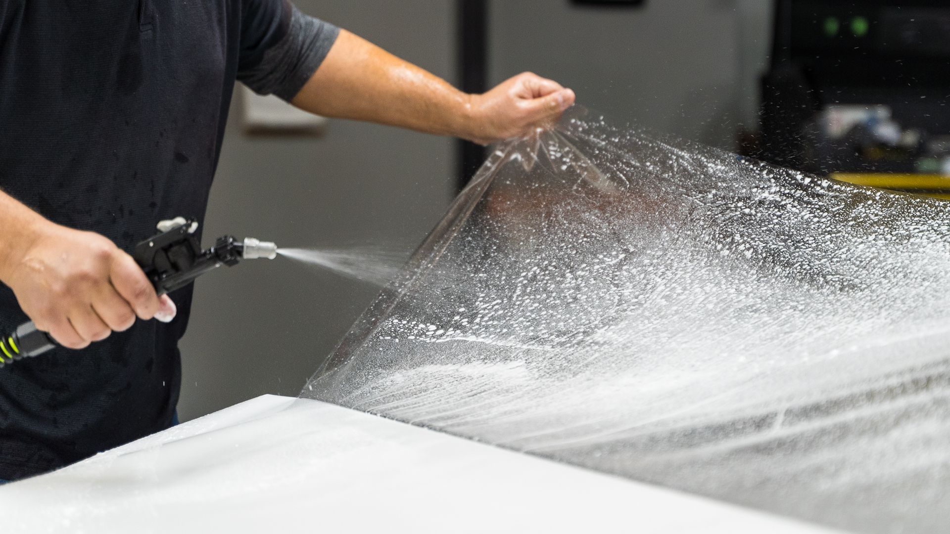 Person spraying water on a large clear film over a white surface.