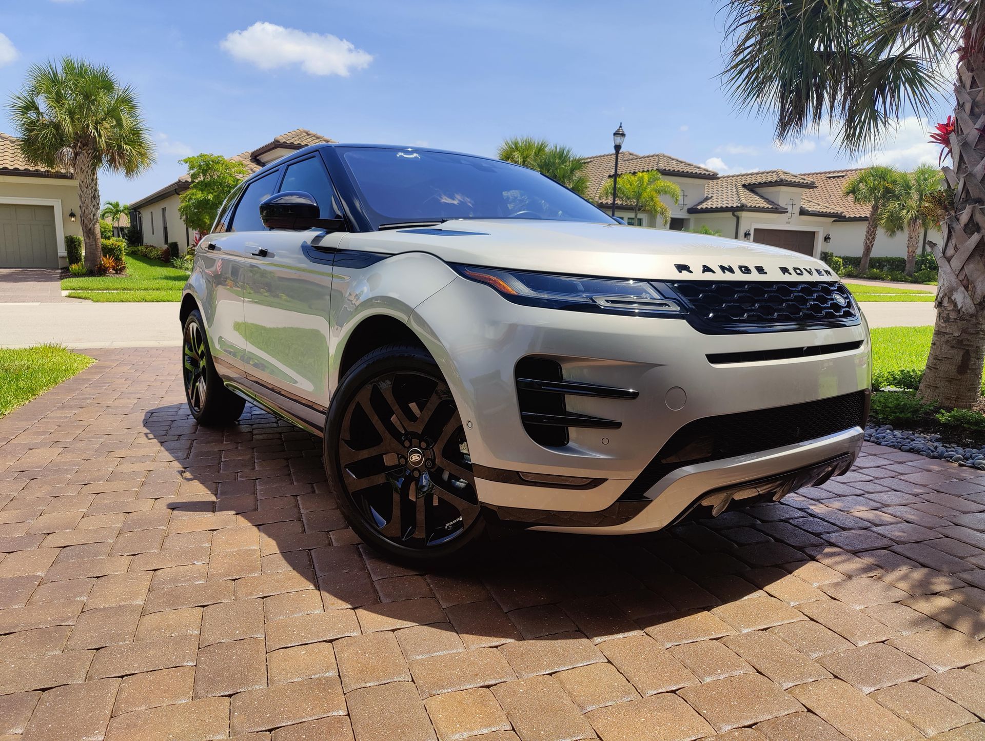 White Range Rover SUV parked on a brick driveway in front of a house.