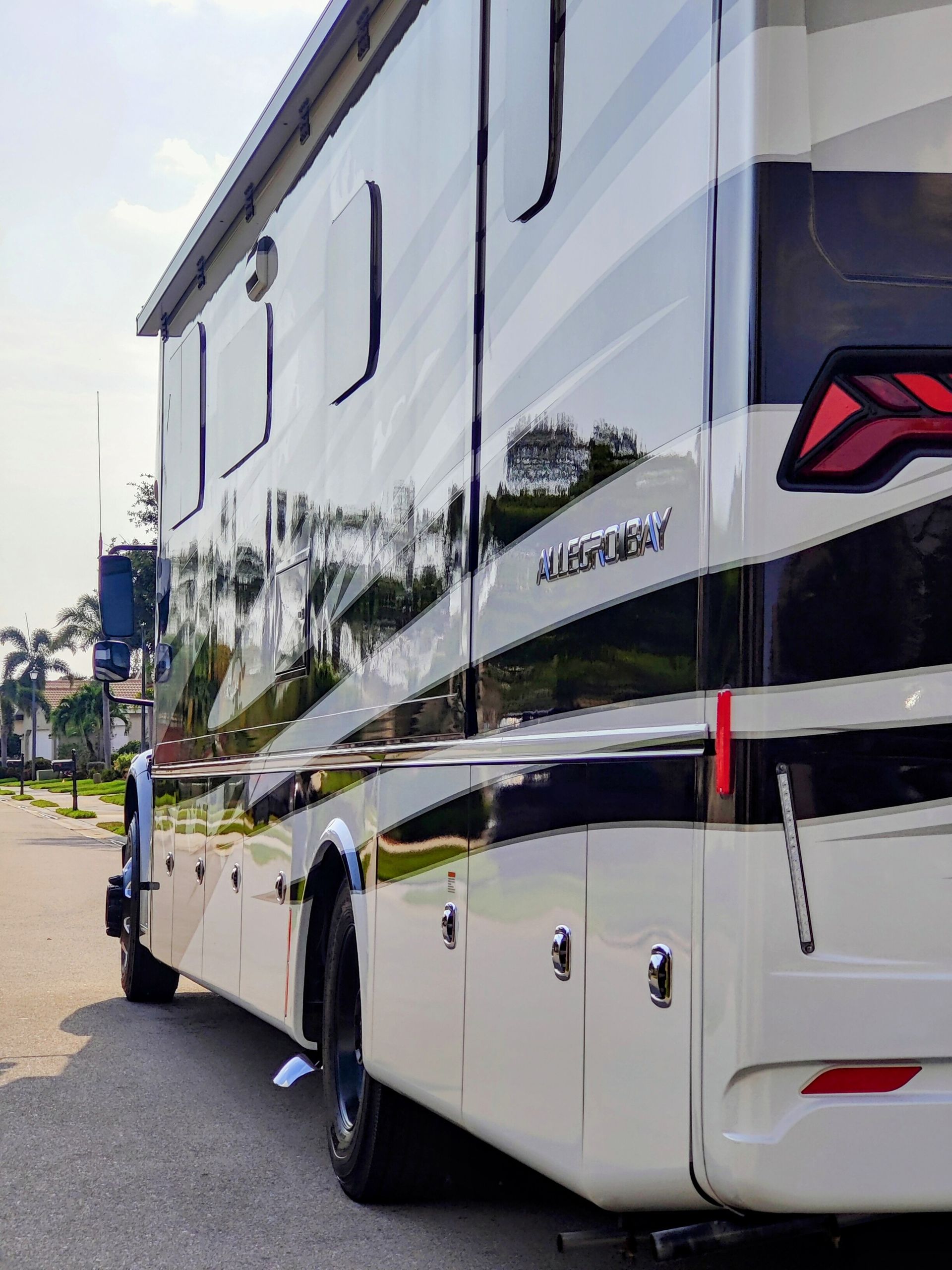Side view of a large RV parked on a street. White and black exterior with storage compartments.