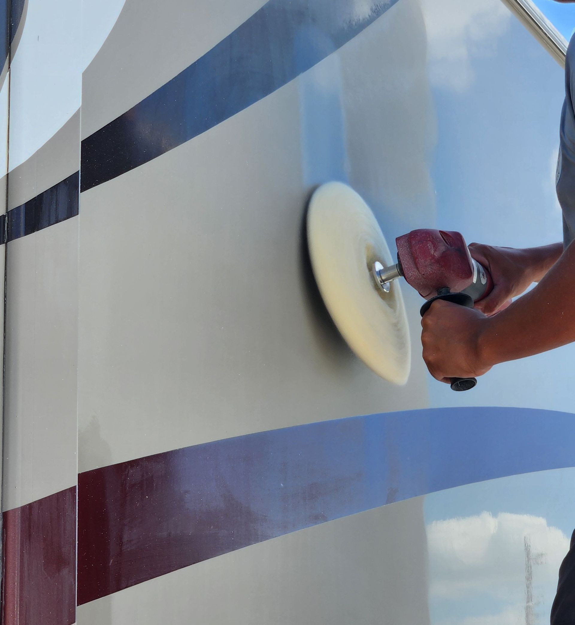 Person using a power buffer on the side of a vehicle.