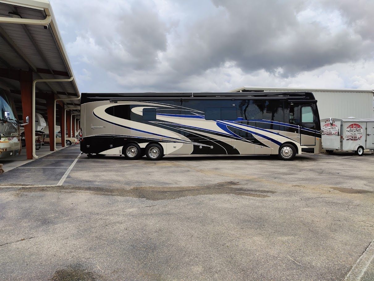 Large, luxurious RV parked under a covered area. It has a silver, black, and blue design.