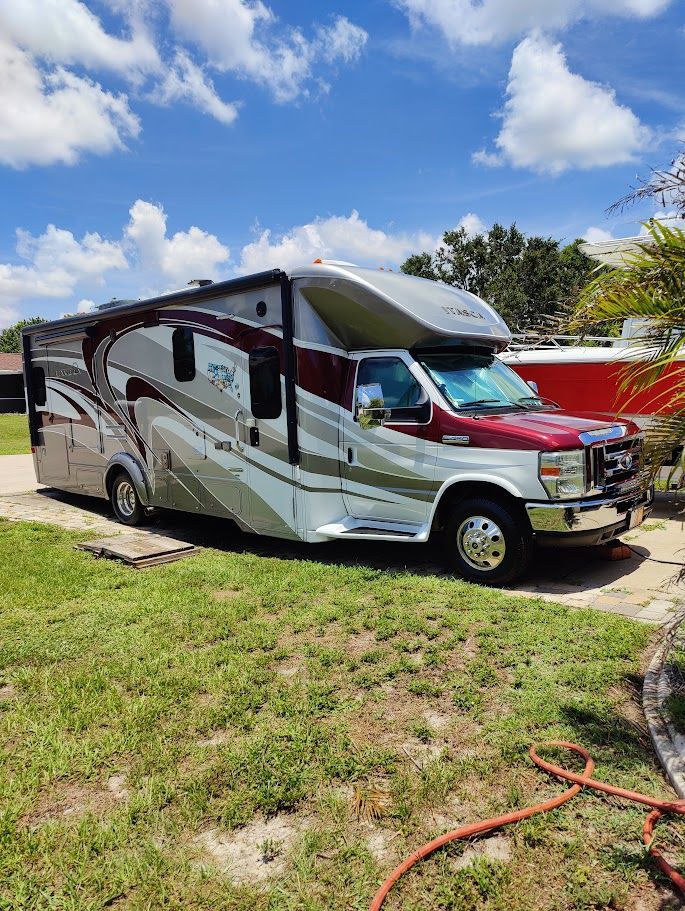 RV parked on grass with a maroon and silver paint job, under a blue sky with fluffy clouds.