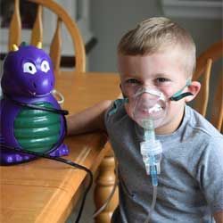 Child wearing a nebulizer mask sits beside a purple toy on a wooden chair